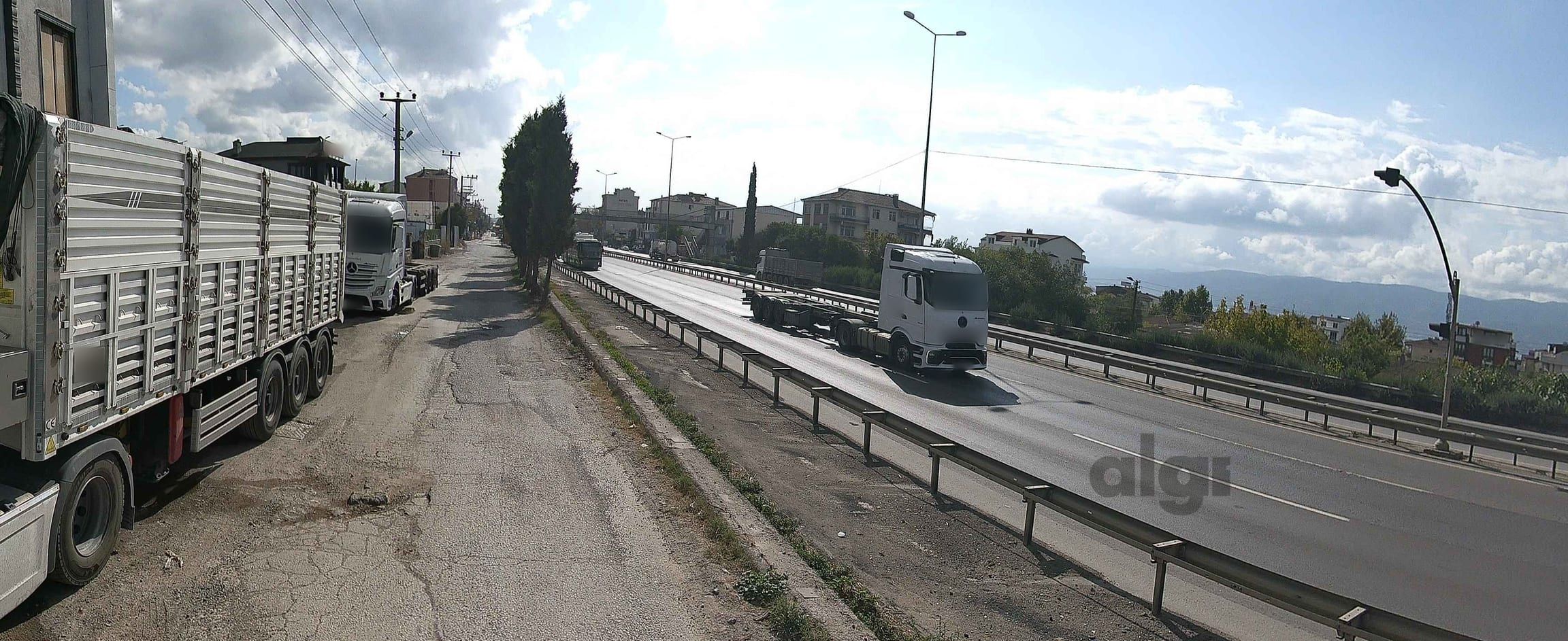Araç kamerasından servis yolu ve ana yol: solda çatlamış ve çökmüş kaplama, ortada bariyer, sağda şeritli ana yol